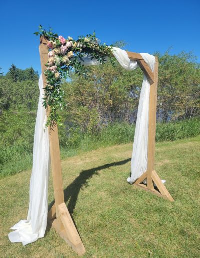 beautiful flowers adorn A wooden Archway with draped white fabric,