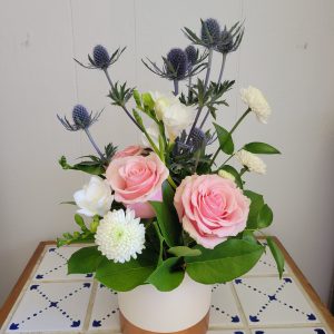 a compact arrangement, in a ceramic white vase. roses and thistles fill out a lovely space.