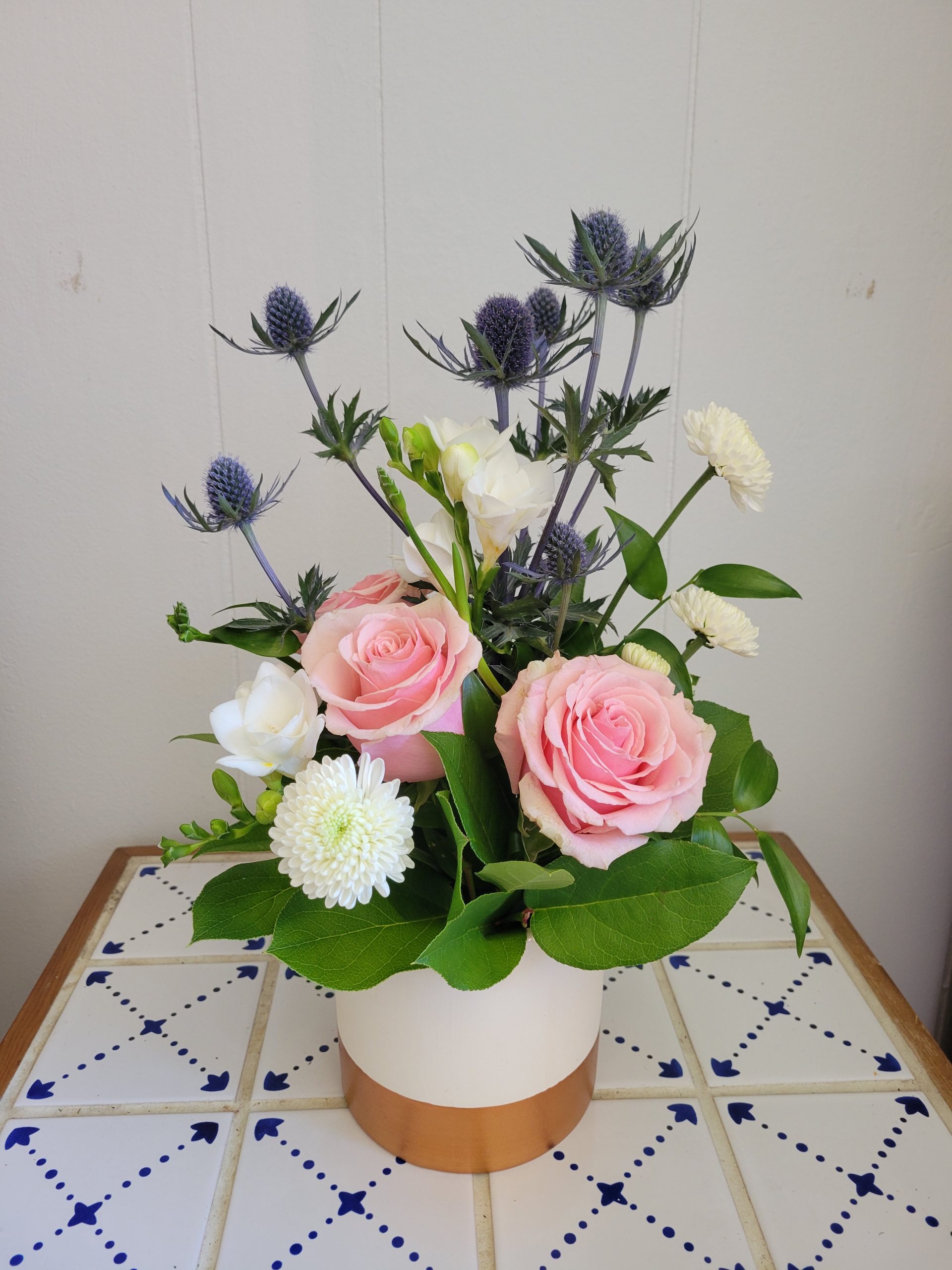 20210818_104039 a compact arrangement, in a ceramic white vase. roses and thistles fill out a lovely space.
